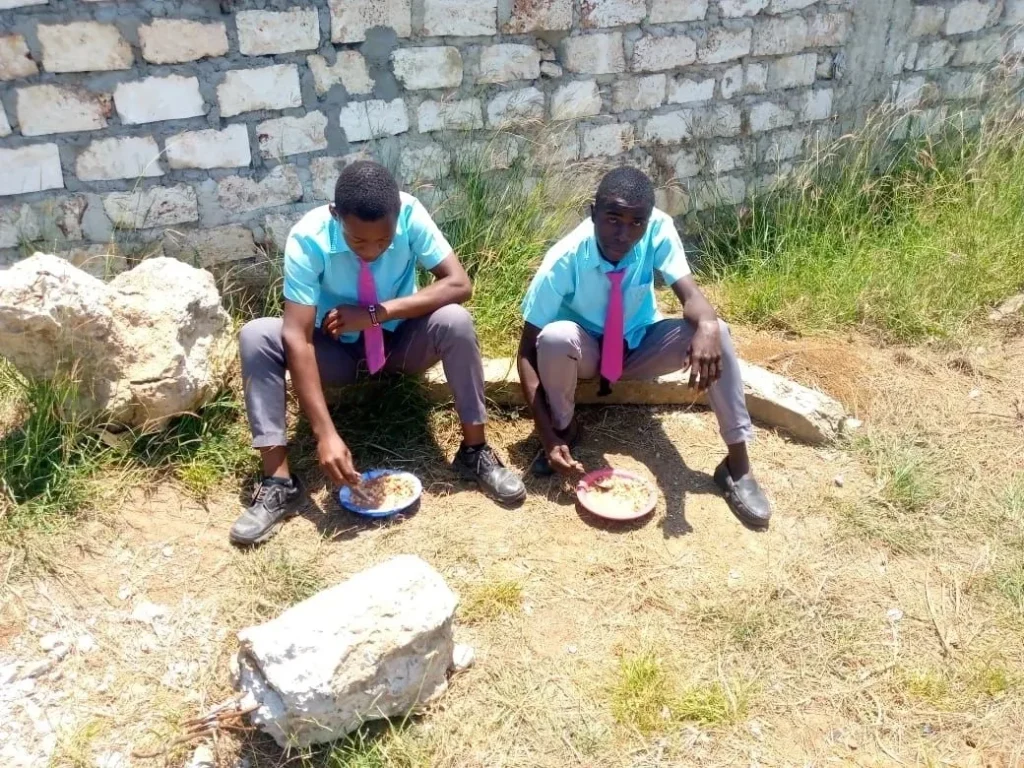Two boys sitting on a bench with plates in front of them.